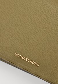 Grønt teksturert lærpengebok med preget gullfarget "MICHAEL KORS" merke nederst. Jevn søm langs kantene.