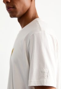 Vit bomull T-shirt med kort ärm och rund halsringning. Har en diskret broderad Adidas-logotyp på ärmen. Slät textur.