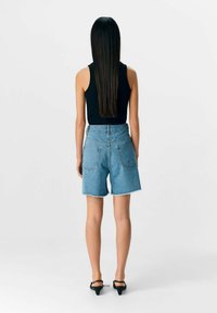 Shorts en denim bleu clair avec taille haute et ourlet effiloché. Comprend deux poches arrière et une coupe droite pour un ajustement décontracté.