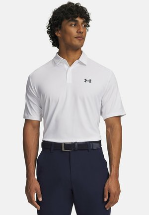 Uomo con polo bianca a maniche corte con logo Under Armour e cintura e pantaloni scuri, che guarda verso sinistra.