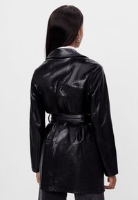 Czarna kurtka z sztucznej skóry z paskiem w talii, długimi rękawami i spiczastym kołnierzem. Posiada gładką teksturę i minimalne detale szwów.