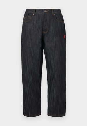 Dark denim jeans with a loose fit. Features a button closure, five pockets, and contrasting orange stitching. Red label on the side.