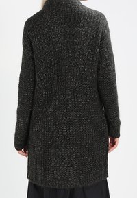 Long, dark gray knitted cardigan with a textured pattern and a high neckline. Features side slits and a relaxed fit for comfort.