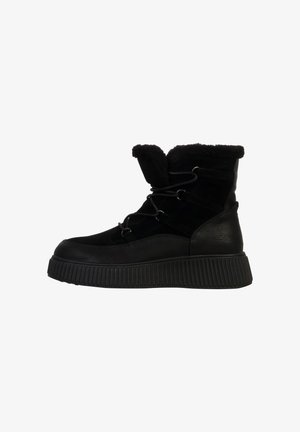 Botines negros con parte superior texturizada, forro de pelaje y punta redonda. Suela de goma gruesa con ranuras horizontales para mayor tracción.