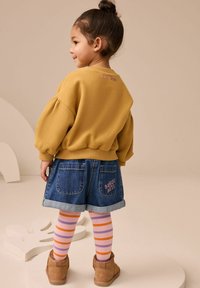 Żółta, teksturowana bluza z bufkami, połączona z dżinsową spódnicą z wywiniętym dołem i haftem "Bunny Bay". Pasiaste legginsy i brązowe buty.