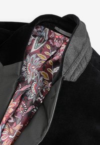 Abrigo de tela negra con cuello gris y forro burdeos con patrón floral, que presenta diseños intrincados en acentos de rosa, verde y amarillo.
