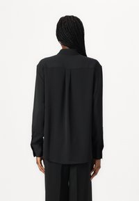 Camisa preta de manga longa com corte reto, detalhes de pregas nas costas e fechos com botão nos punhos, feita de um tecido suave.