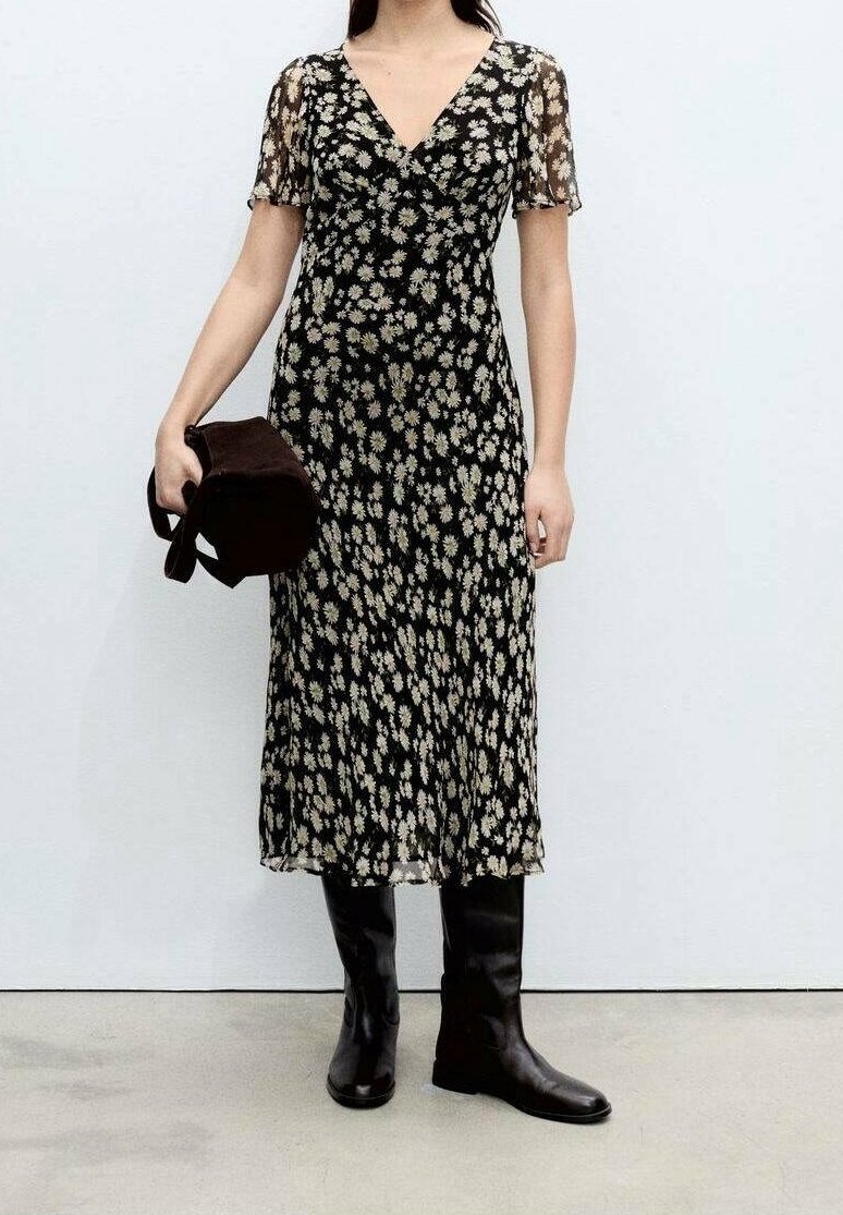 Vestido midi negro con estampado floral y mangas cortas de encaje, con escote en V y silueta fluida. Combinado con botas negras hasta la rodilla y un bolso marrón.