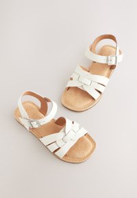 Sandales en cuir blanc avec brides à la cheville, boucles argentées et design noué à l'avant sur semelles rembourrées couleur fauve.