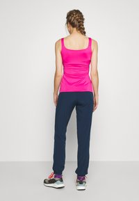 Bright pink sleeveless athletic top paired with navy athletic pants. The top features a fitted design, while pants have cuffs and a relaxed fit.