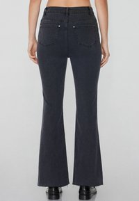 Schwarze, ausgestellte Jeans mit hoher Taille, ausgestattet mit zwei Gesäßtaschen und rohen Säumen. Hergestellt aus Denim, mit glatter Textur und dunkler Farbe.