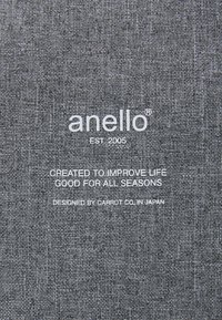 Šedá tkanina s texturovaným vzorem. Obsahuje bíle tištěný text: "anello", rok založení a atribuci designu. Jednoduchý, moderní design.