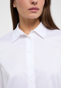 White button-up shirt made of smooth fabric, featuring a classic collar, a row of buttons, and a fitted design.