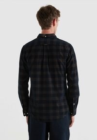 Camisa de franela a cuadros azul marino con mangas largas, cuello abotonado y dobladillo redondeado, con dos puños abotonados y un yugo trasero.