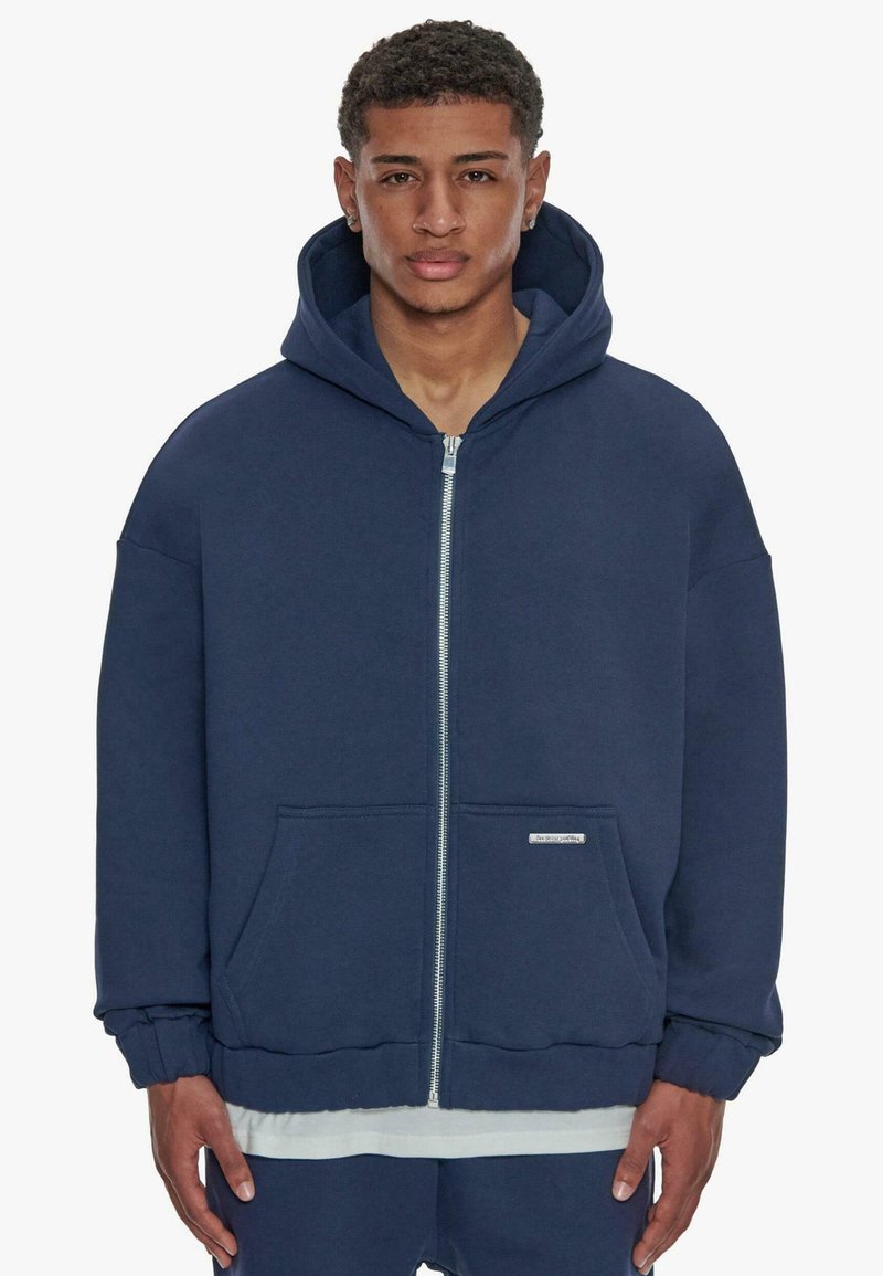 Navyblauer Zip-Hoodie aus dickem Baumwollmaterial. Verfügt über eine Fronttasche, gerippte Bündchen und eine gefütterte Kapuze mit einem schlichten Logo-Akzent.
