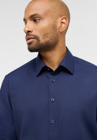 Navy-blaues Button-up-Hemd mit strukturiertem Muster, Umlegekragen und passenden Knöpfen, zeigt eine Nahaufnahme des Designs des Hemdes.