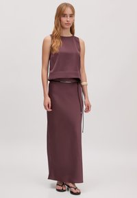 Bordeaux satijnen twee-delige outfit met een mouwloze top en een vloerlange rok, voorzien van een zwarte strikceintuur en een minimalistisch ontwerp.