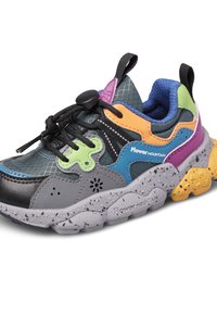 Zapatilla de montaña colorida con flor, cordones negros, suela gris moteada y detalles en verde, naranja, azul, púrpura y amarillo, logo lateral visible.