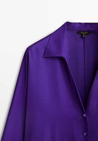 Lilla skjorte i satin med krave, lange ærmer og knaplukning. Glat tekstur, blank finish og diskret glans fremhæver stoffet.