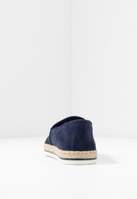 Navyblå mocka slip-on skor med en beige vävd jute-mellansula och vit gummisula. Rundad baksida med mjuk textur och minimalistisk design.
