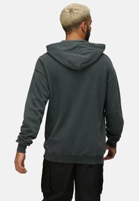 Sudadera con capucha de color gris oscuro, de corte relajado, con puños y dobladillo acanalados, hecha de material suave. Detalles de costura visibles en la parte trasera.
