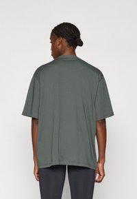 Veľká košeľa s krátkym rukávom v tmavozelenej bavlne, so zaobleným výstrihom a voľným strihom. Hladká textúra a rovný lem.