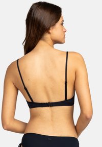 Černý bikiny top s nastavitelnými tenkými popruhy, s háčkovým zapínáním na zadní straně, hladkou strukturou a minimalistickým designem, který ukazuje pohled ze zad.