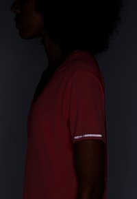 Pink athletic shirt with a v-neck, featuring a reflective accent on the short sleeve. Material appears lightweight and breathable.