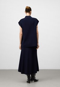 Completo lavorato a maglia di colore blu navy composto da una maglietta a maniche corte e una gonna lunga, realizzato in un tessuto morbido con una texture liscia. Stivali alti e aderenti neri.