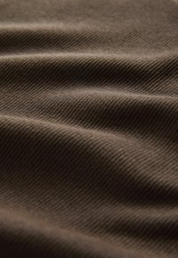 Gros plan sur un tissu marron avec une texture diagonale fine en relief et des plis doux créant des ombres et des reflets délicats.