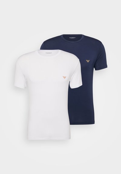 Dvě trička s krátkým rukávem, jedno bílé a jedno tmavě modré, vyrobená z měkké látky. Každé má na hrudi malé logo v kontrastních barvách.