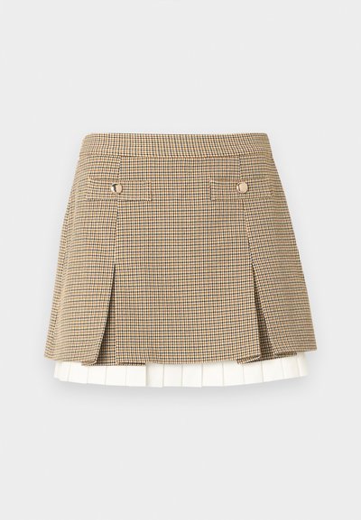 Jupe courte à carreaux avec des motifs beige, noir et blanc, comprenant deux rabats avant boutonnés et un détail à l'ourlet plissé blanc.