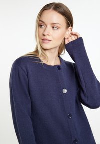 Granatowy sweter robiony na drutach o teksturowanej tkaninie, okrągłym dekolcie i trzech dużych guzikach. Posiada szerokie mankiety i luźny krój.
