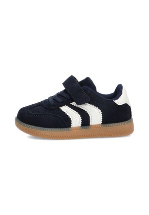 Zapatilla deportiva azul marino para niño con rayas blancas, tira de velcro ajustable, detalles de cordones y suela de goma marrón.