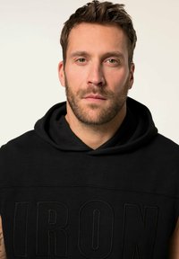 Schwarzer ärmelloser Hoodie mit einer vorderen Kängurutasche, der ein geprägtes "IRON"-Design aufweist. Glatte Textur, verstellbare Kapuze, minimalistische Stil.