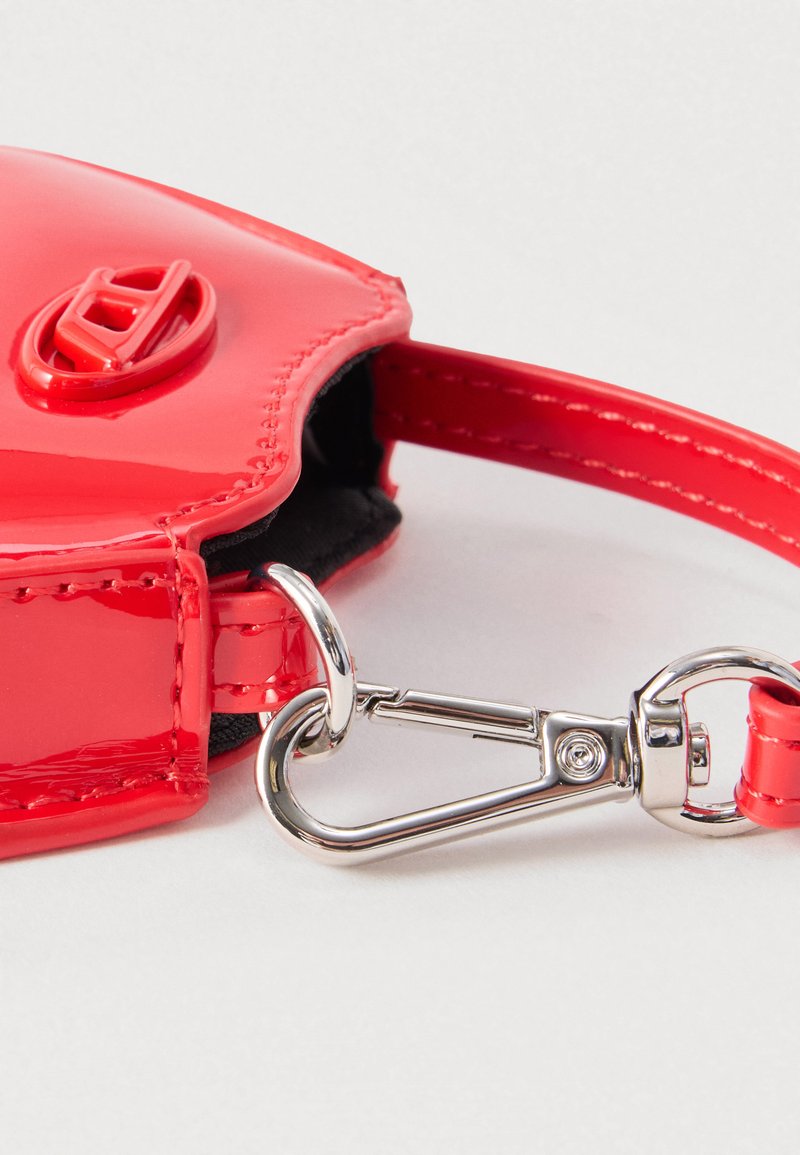 Close-up van een rode polsband van lakleer met een zilveren metalen gesp en draaivergrendelknop op een etui.