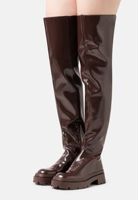 Botas de muslo altas en color marrón brillante con una suela de plataforma gruesa, presentando una cremallera lateral para un ajuste fácil y una textura suave y elegante.