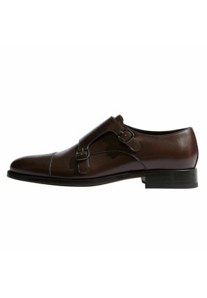 Zapato de vestir de cuero marrón con una textura suave, que cuenta con dos hebillas ajustables y una puntera redondeada. Tacón plano y detalle de costura en contraste.