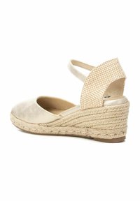 Zapato de cuña beige de espadrille con un respaldo texturizado, tirante en el tobillo y suela de yute trenzado. Material liso en la punta con forma redondeada.
