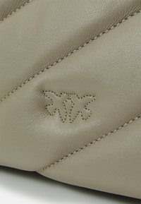 Beige lærveske med diagonalt quiltet design, som har sømde detaljer og preget logo på forsiden. Glatt tekstur med fine detaljer.