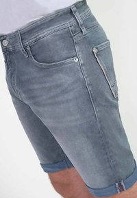 Grijze denim shorts met een slim fit, omgeslagen boorden, zijzakken en een ritssluiting detail op één dij. Gladde textuur met minimale vervaging.