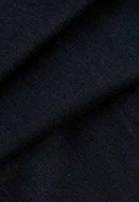 Close-up van donkerblauwe denimstof, gevouwen om textuur en weefpatroon te tonen.