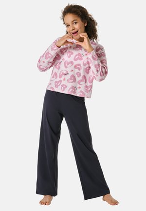 Un haut rose clair à manches longues avec des motifs en forme de cœur, associé à un pantalon noir ample. La tenue présente des textures douces et un design décontracté.
