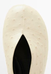 Scarpa in pelle crema con texture a puntini in rilievo, apertura a forma di mandorla e interno nero. Finitura liscia, punta arrotondata e design minimalista.