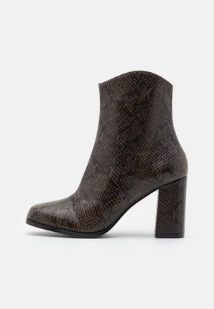 Botte ankle en simili cuir serpent marron avec un bout carré, un haut talon bloc et une texture lisse. Design épuré avec un haut légèrement courbé.