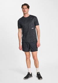 Czarna koszulka sportowa z teksturowanym wzorem, w zestawieniu z czarnymi szortami. Oba elementy mają małe logo. Całość uzupełniają czarne i szare buty sportowe.