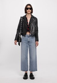 Giacca in pelle nera cropped, blusa floreale, jeans a gamba larga azzurri e mocassini neri spessi. Gli occhiali da sole completano il look.