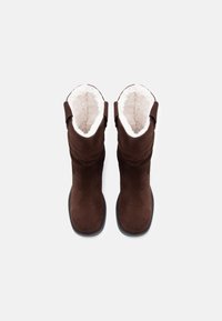 Bottes en suède marron avec une douce doublure en fourrure blanche, bout arrondi, design mi-mollet et détails cousus sur les côtés. Semelles en caoutchouc.