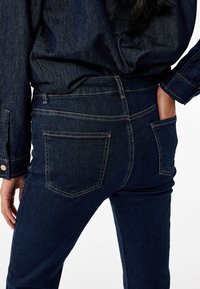 Donkerblauwe denim jeans met een slim fit ontwerp, twee achterzakken met stiksel details en een middenlopende taille.