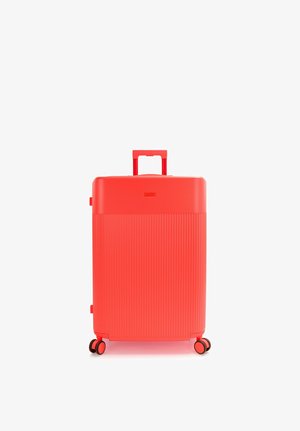 Valise rigide rouge vif avec quatre roues pivotantes et une poignée télescopique déployée sur fond blanc.